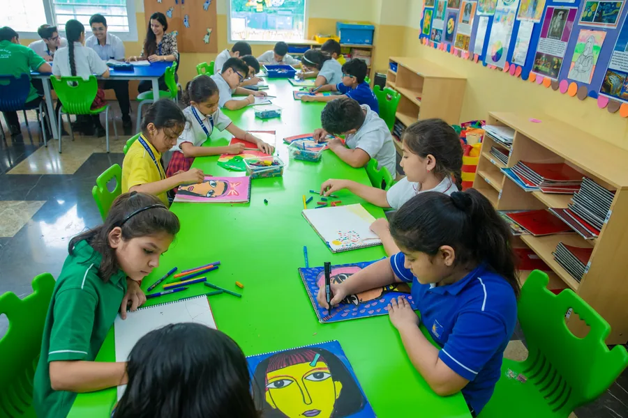 Pupils drawing and painting along a long green table, finished portraits propped behind them