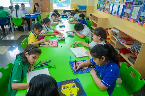 Pupils drawing and painting along a long green table, finished portraits propped behind them