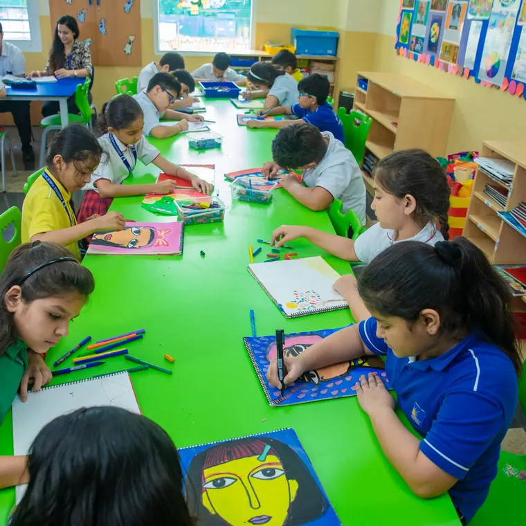 Pupils drawing and painting along a long green table, finished portraits propped behind them