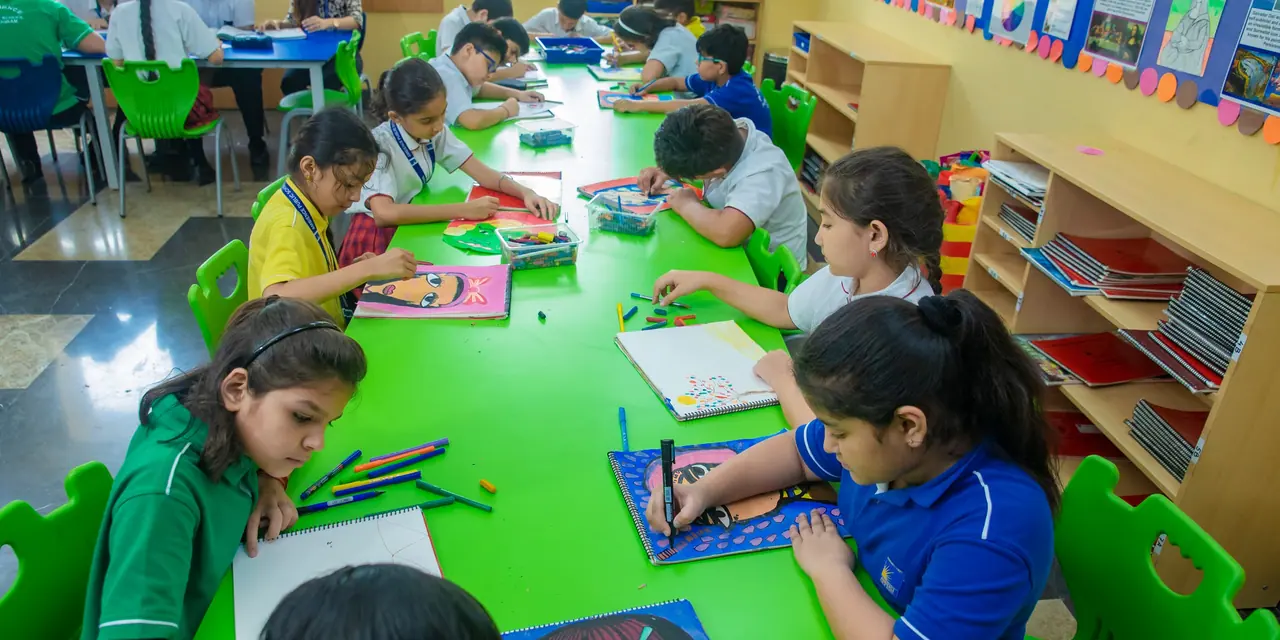 Pupils drawing and painting along a long green table, finished portraits propped behind them