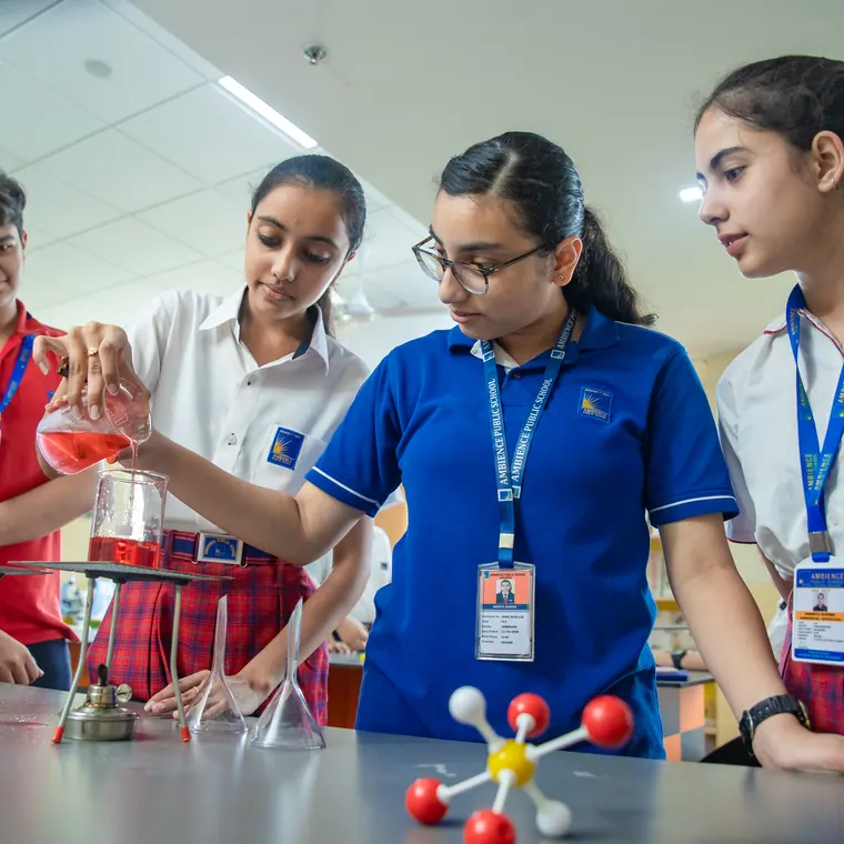 Senior girls at work in the chemistry laboratory, one pouring an orange solution
