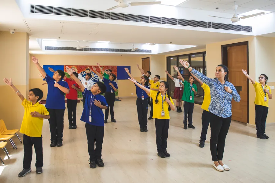 A teacher leading pupils in an arms-out movement exercise in a bright open studio