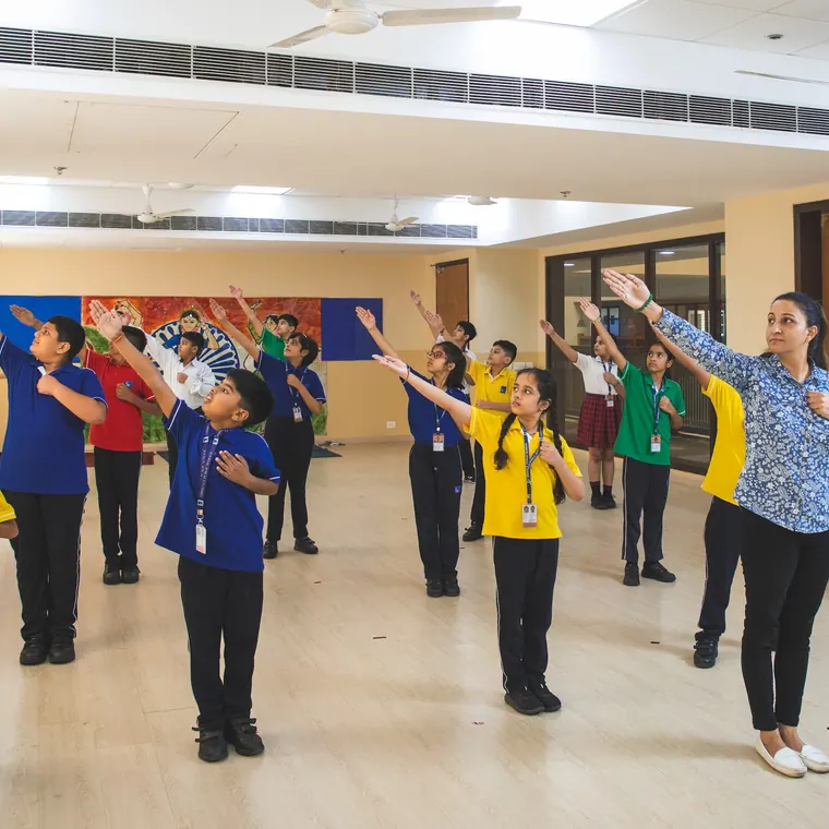 A teacher leading pupils in an arms-out movement exercise in a bright open studio