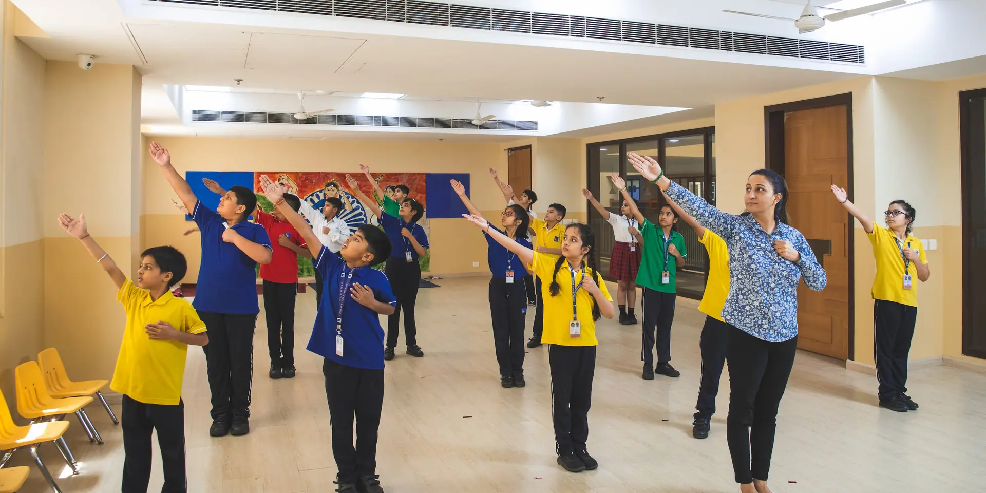 A teacher leading pupils in an arms-out movement exercise in a bright open studio