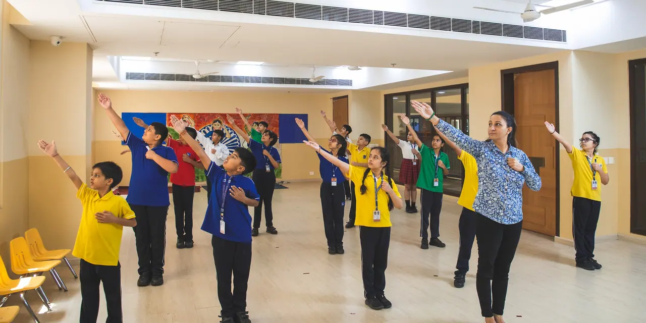 A teacher leading pupils in an arms-out movement exercise in a bright open studio