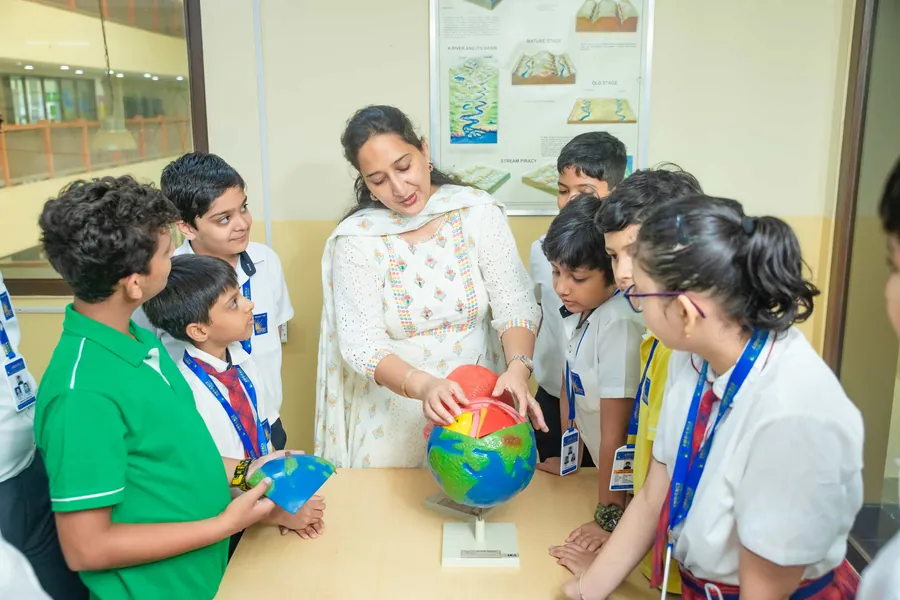 A teacher pointing at a globe while pupils crowd in to look