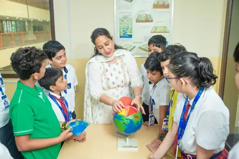 A teacher pointing at a globe while pupils crowd in to look