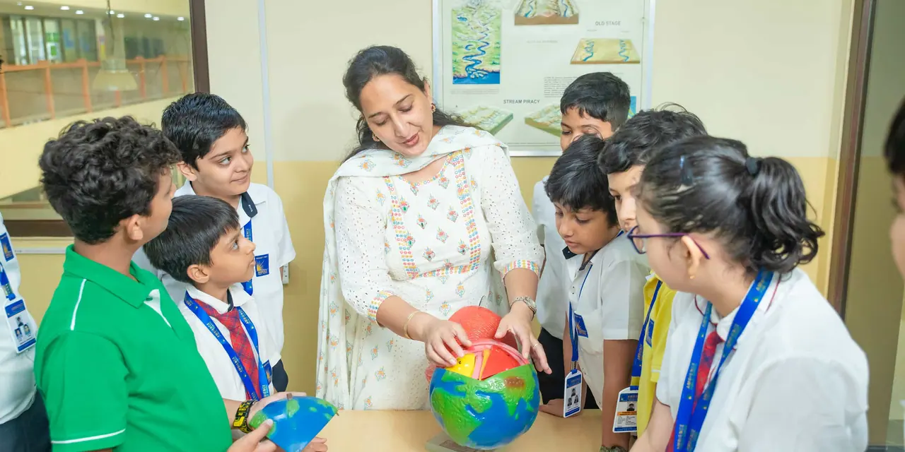 A teacher pointing at a globe while pupils crowd in to look
