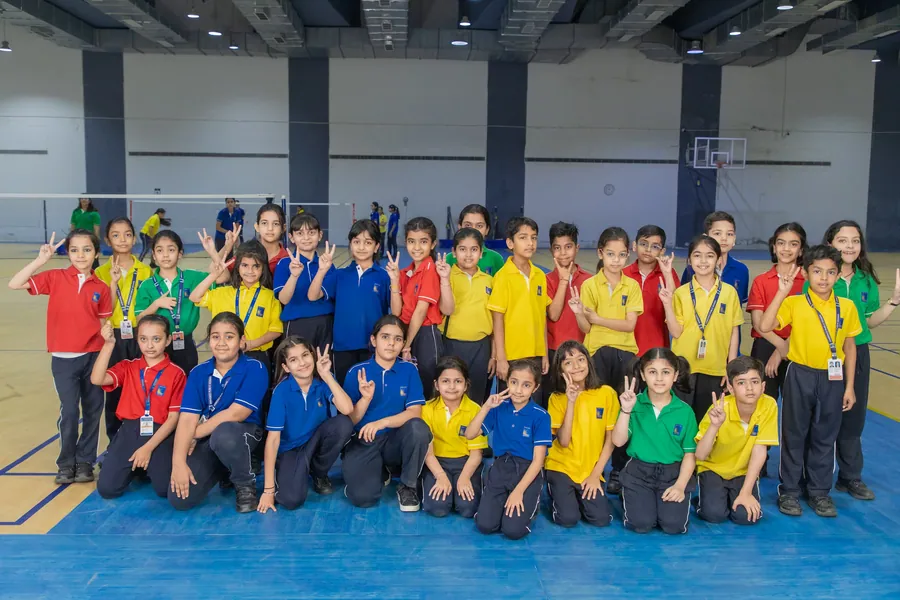 A large group of primary pupils in house colours on the indoor sports hall floor, many waving