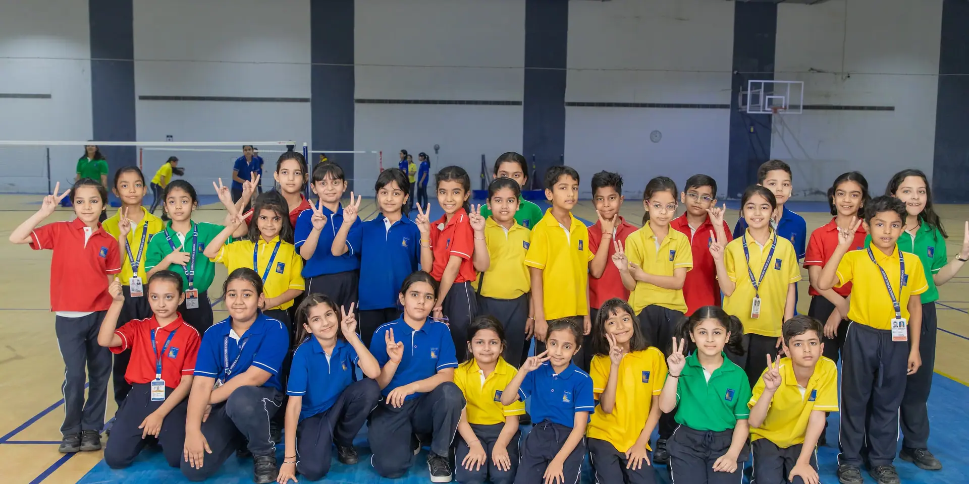 A large group of primary pupils in house colours on the indoor sports hall floor, many waving