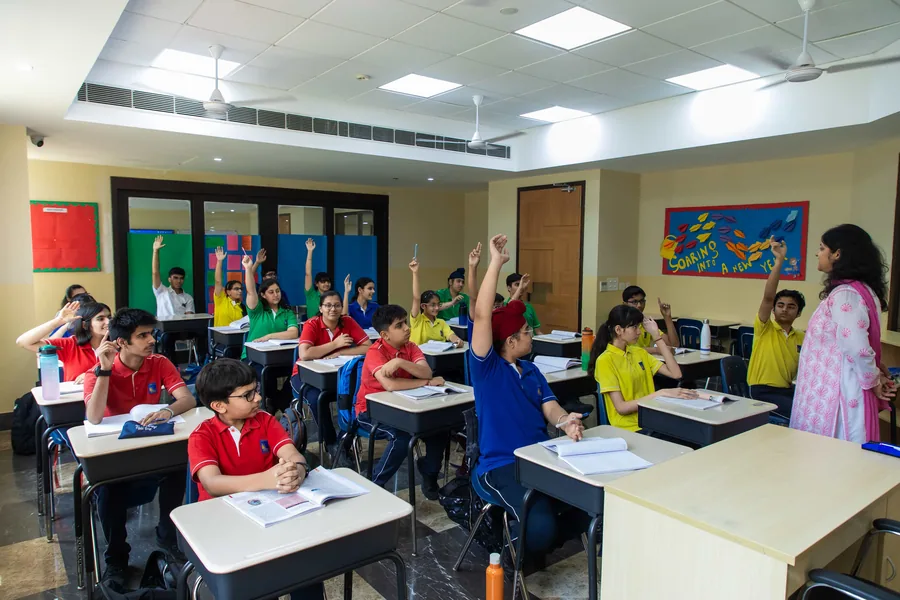 A classroom of pupils in house colours with their hands up to answer, the teacher at the side