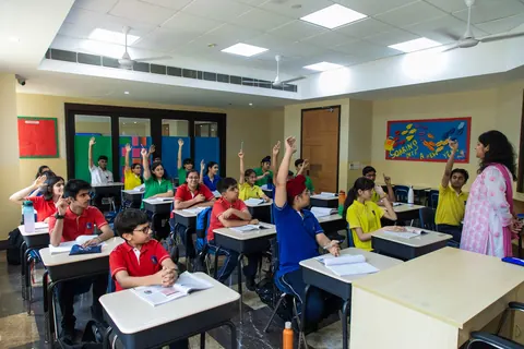 A classroom of pupils in house colours with their hands up to answer, the teacher at the side