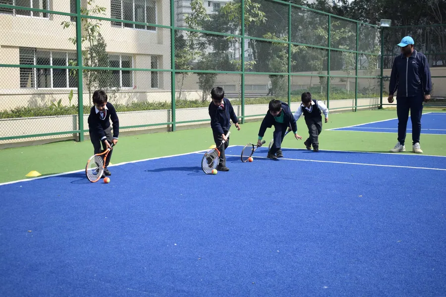 Younger pupils in navy tracksuits practising hockey drills on the blue synthetic court