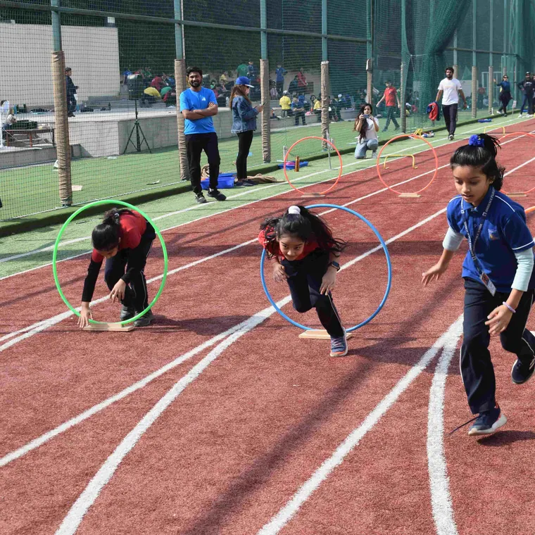 Girls stepping through red, green and blue hoops laid along the red running track