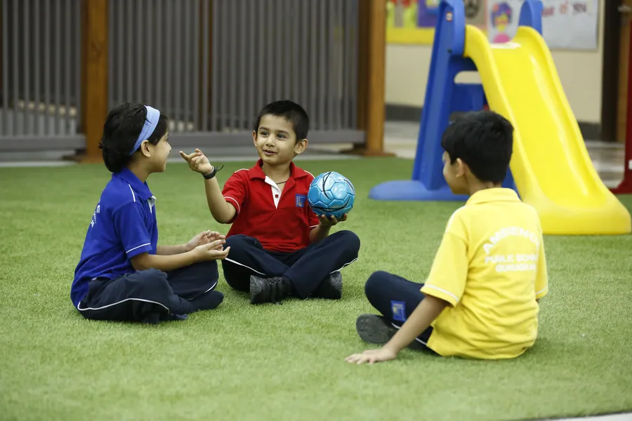 Three boys in blue, red and yellow house shirts sitting on the turf passing a ball