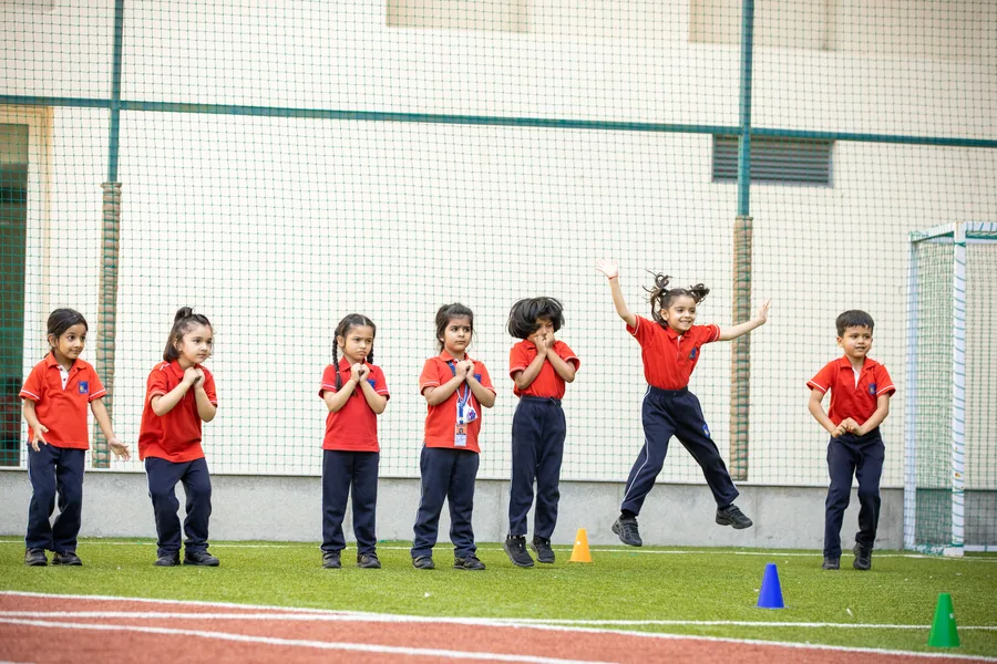 A line of children in red house shirts on the turf, one caught mid-leap with both arms flung wide