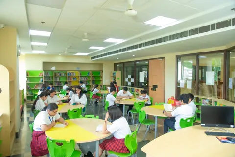 Pupils reading at round yellow and green tables among tall library shelves