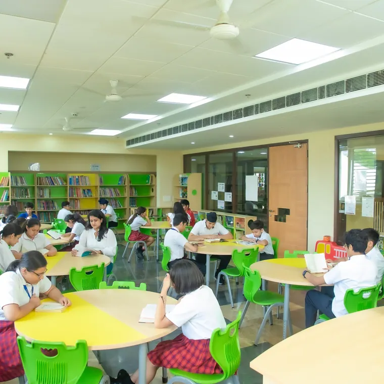 Pupils reading at round yellow and green tables among tall library shelves