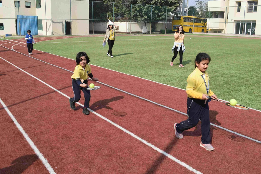 Children in yellow house shirts running a ball-and-racket relay on the track