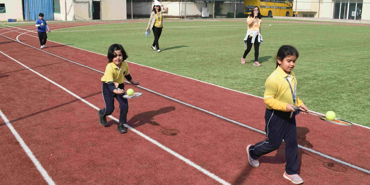 Children in yellow house shirts running a ball-and-racket relay on the track