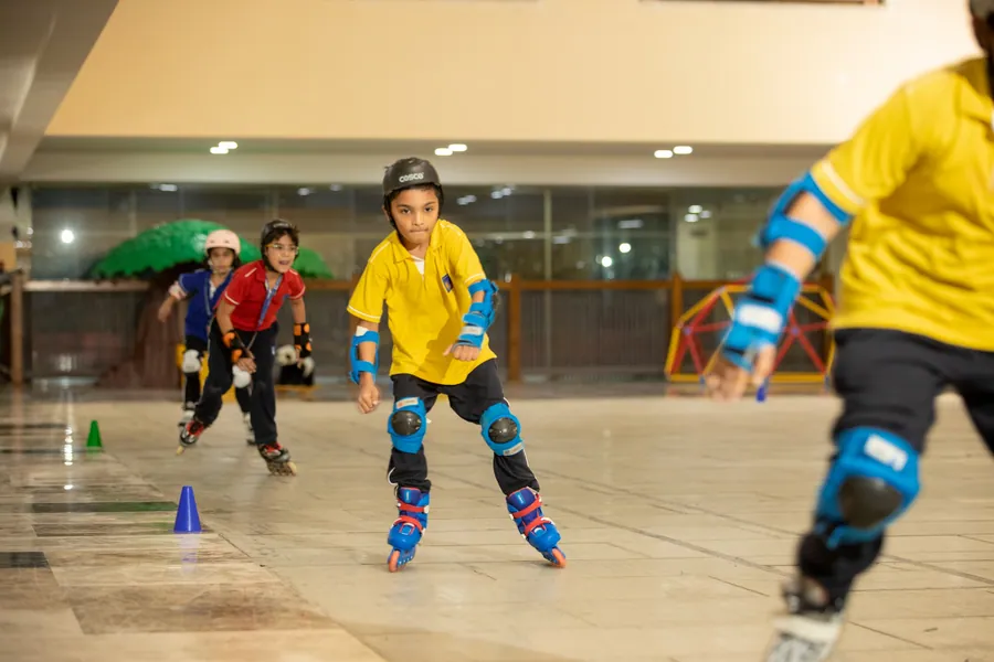 A child in a yellow shirt, helmet and pads skating towards the camera between cones