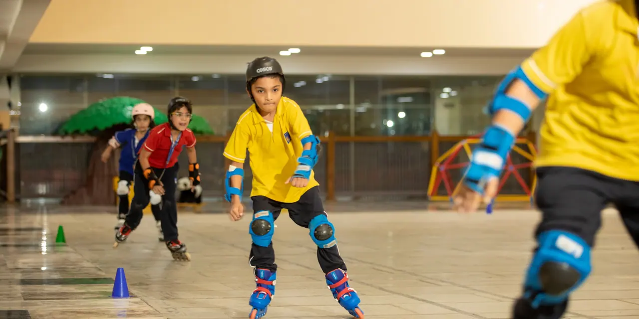 A child in a yellow shirt, helmet and pads skating towards the camera between cones