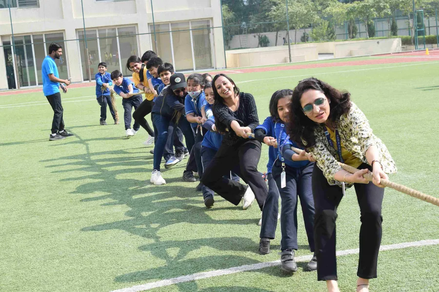 Pupils and teachers leaning back hard on the rope in a tug of war across the green turf